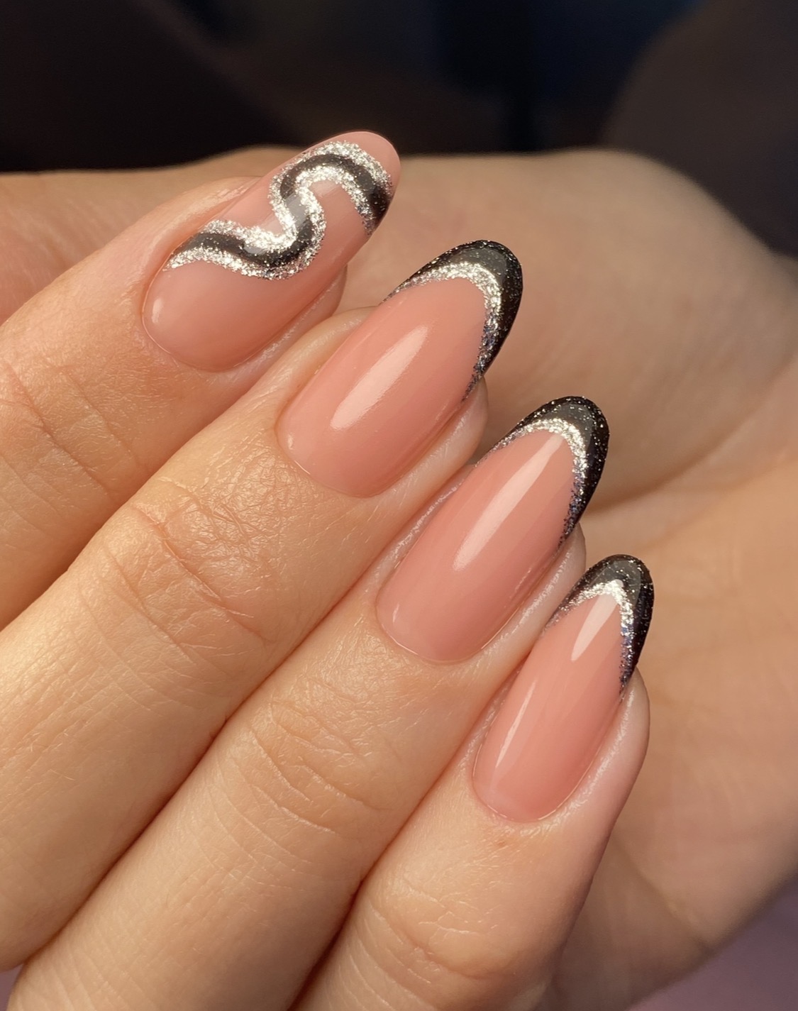 Nude nagels met een zwarte glitter-French en een zilveren swirl