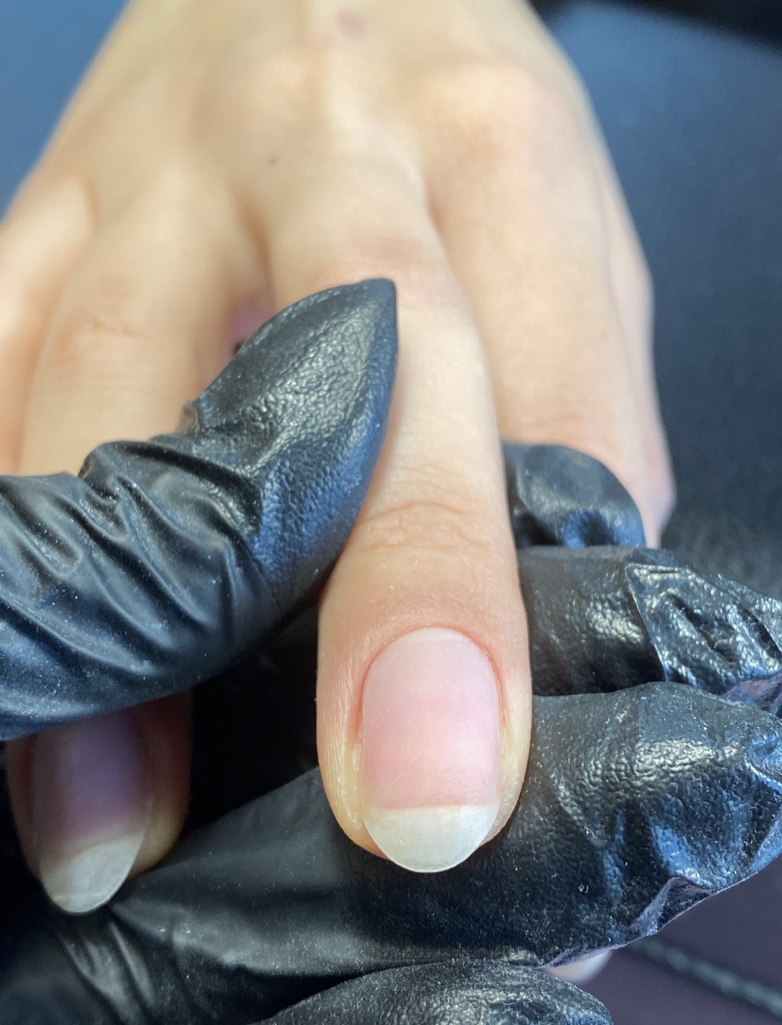 Een verzorgde natuurlijke nagel, vastgehouden met een zwarte handschoen