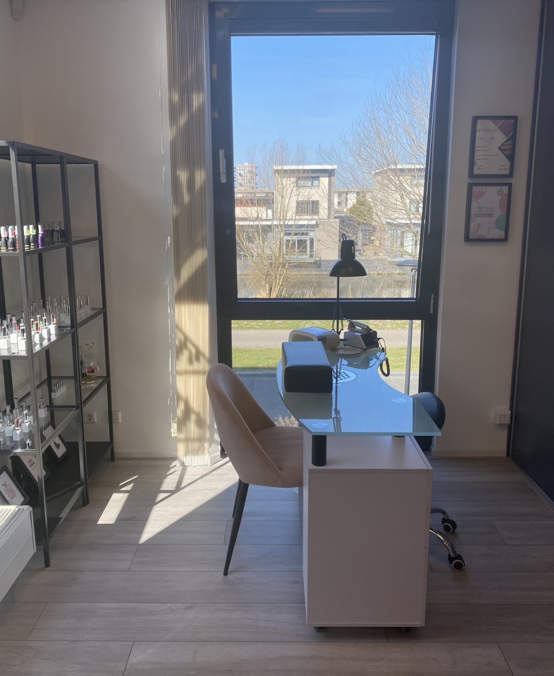 De nageltafel met matglazen blad voor een groot raam, met een blush fluwelen stoel