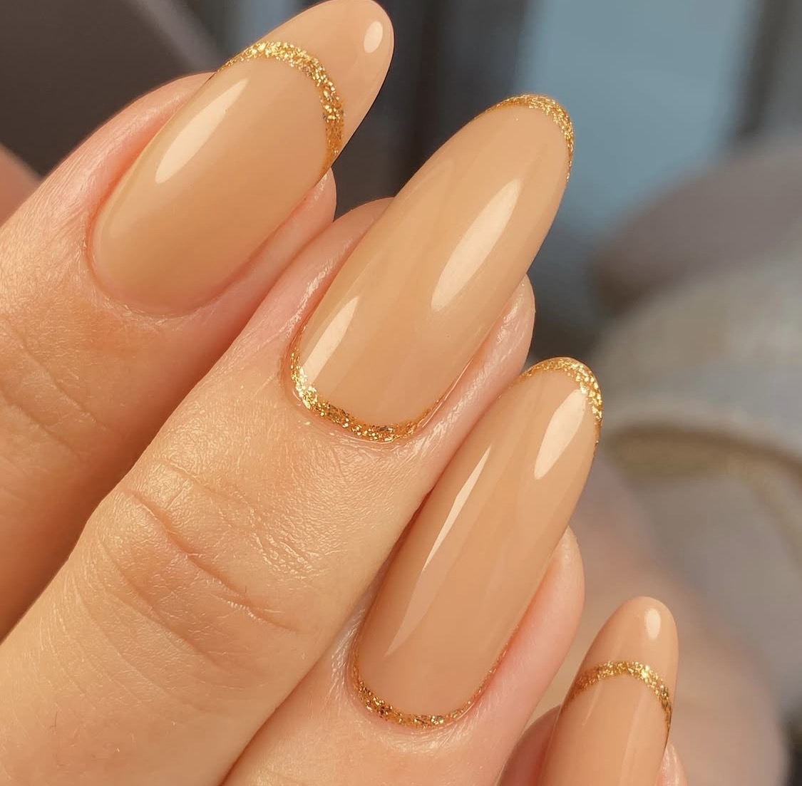 Lange amandelvormige nagels in nude met een gouden glitterrand